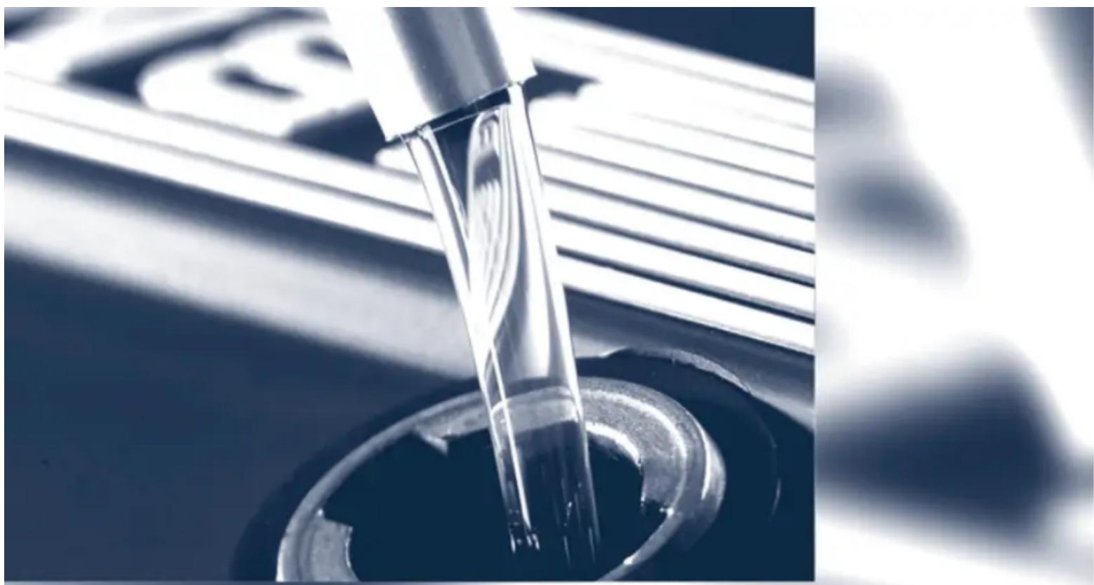 Close-up of a metallic tool tip dispensing liquid into a circular container (no visible text or symbols)