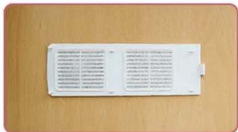 Scanned image of a white electronic device with printed text on its surface, placed on a wooden surface.