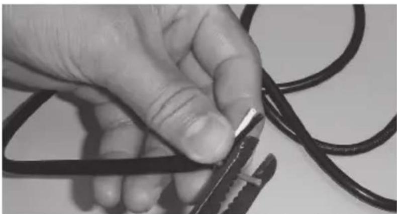 Close-up of a hand holding a pair of black wires with metal clips, no visible text or symbols