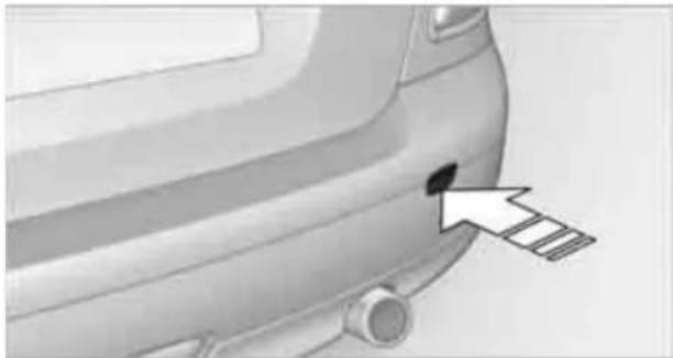 Side view of a car's front bumper with a white arrow pointing to a small black dot on the rear (no text or symbols visible)