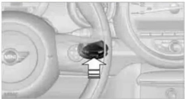 Close-up of a car interior showing a dark circular object with an arrow pointing to it, surrounded by other vehicle parts (no visible text or symbols)