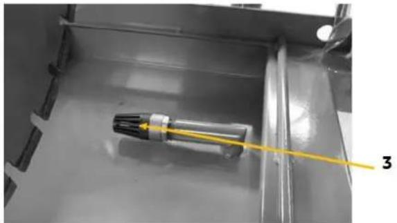 Close-up of a mechanical component with a yellow wire and label '3' pointing to it, placed on a metallic surface (no readable text or symbols beyond label)