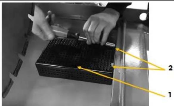 Black-and-white photo of hands using a tool on a perforated metal tray, with numbered annotations pointing to components 1 and 2.
