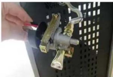 Close-up of a hand holding a tool next to a mechanical component mounted on a black panel (no visible text or symbols)