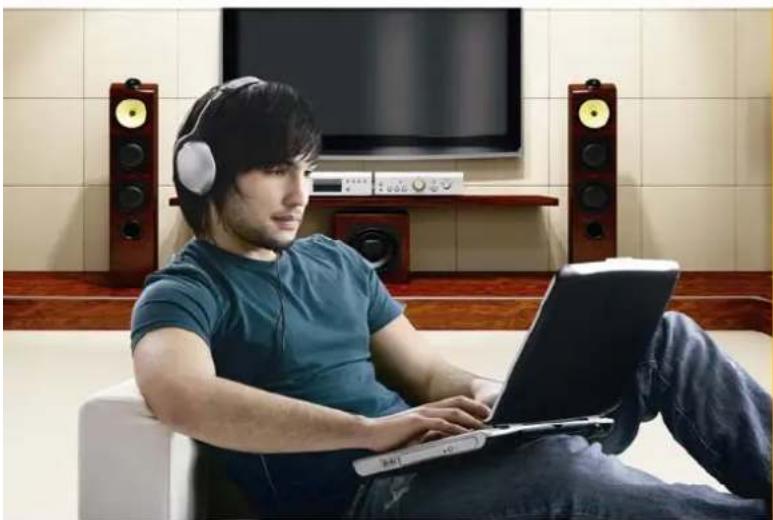 Man wearing headphones while using a laptop in a living room with TV and audio equipment (no visible text or symbols)