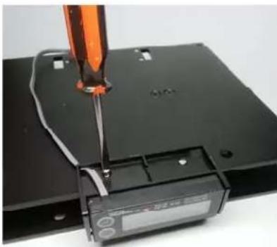 Close-up of a screwdriver inserted into a black electronic device with a display panel (no visible text or symbols)