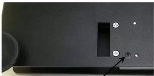 Close-up of a black electronic device panel with a rectangular cutout and two circular holes, one marked with an arrow (no text or symbols visible)