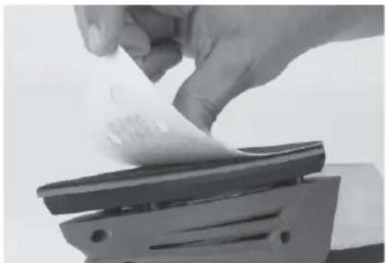 Close-up of a hand holding a sheet of paper over a mechanical clip (no visible text or symbols)