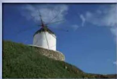 White windmill on a grassy hill under a blue sky with scattered clouds (no text or symbols visible)