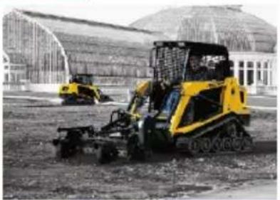 Two yellow tracked excavators operating in a construction site with large greenhouses in the background (no visible text or symbols)