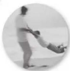 Black-and-white circular photo of a person pulling a baby on a beach (no text or symbols visible)