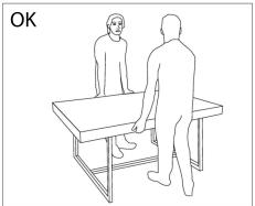 Line drawing of two people standing at a table, one facing forward and the other seated (no text or symbols)