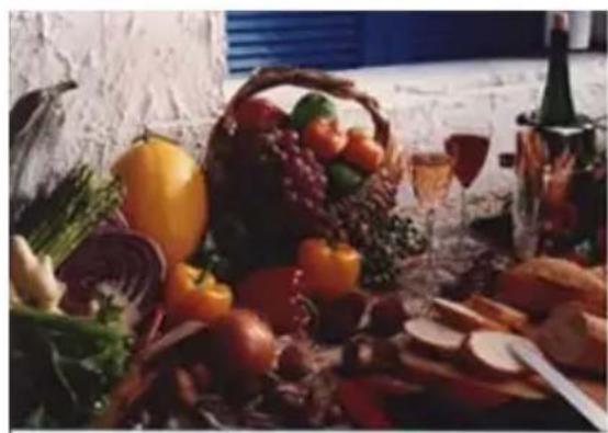 Still life arrangement of assorted fruits and vegetables on a table, with wine bottles and glass in background (no text or symbols visible)