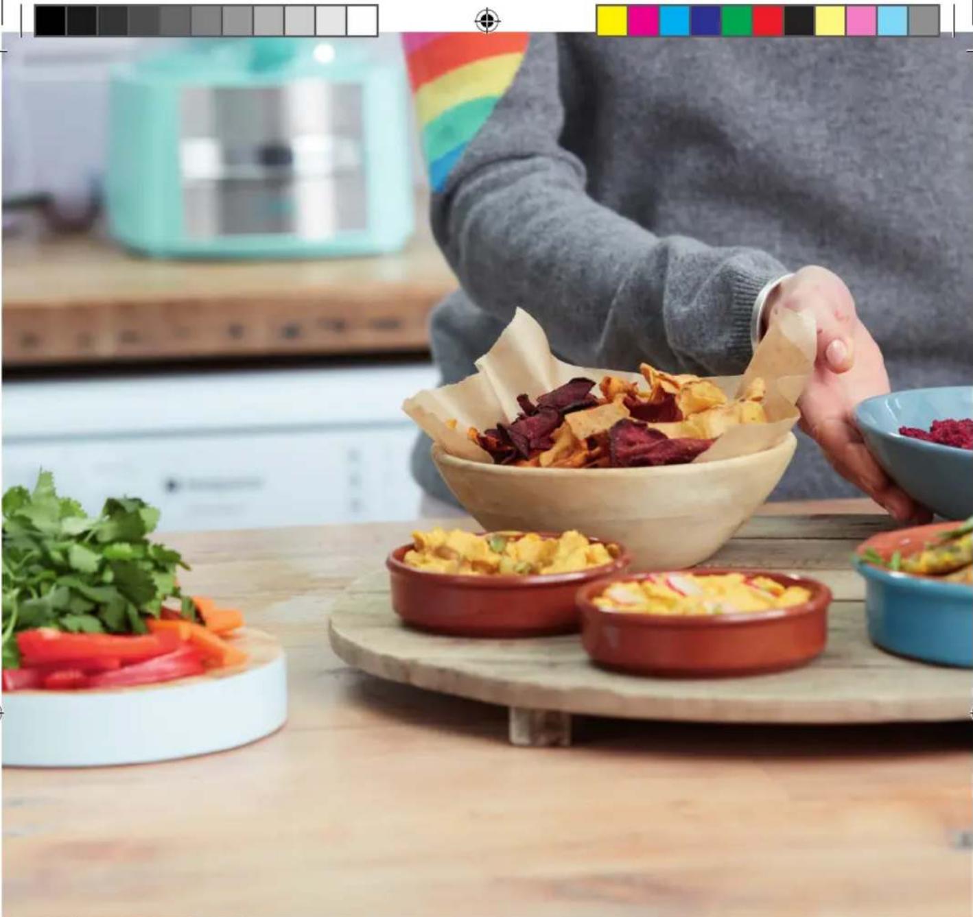 Person preparing food in a kitchen, placing a paper liner into a bowl of dried fruit and colorful dishes on a wooden board (no visible text or symbols)