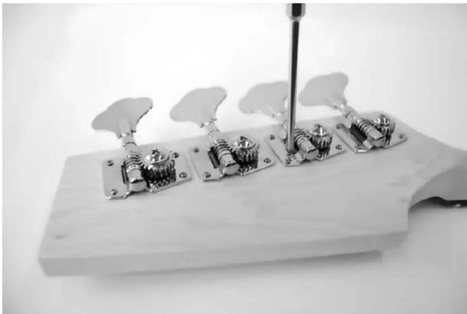 Black-and-white photo of a guitar headstock with four electric guitar blocks and a tuning fork (no text or symbols visible)