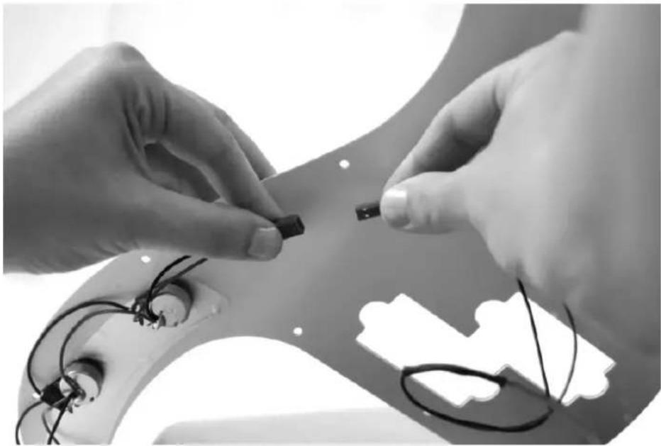 Close-up of hands assembling electronic components on a curved surface, with wires and a cut-out gear-like shape visible (no text or symbols)
