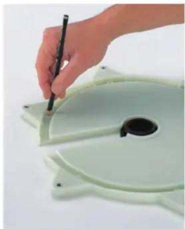 Hand holding a pen next to a light green plastic disc with a central hole (no text or symbols visible)