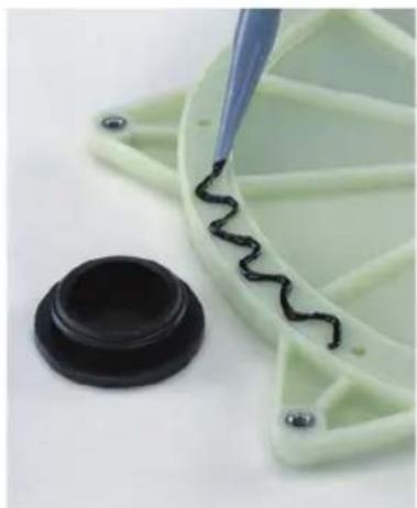Close-up of a green plastic container with black wavy lines being inserted, alongside a black circular base (no text or symbols visible)