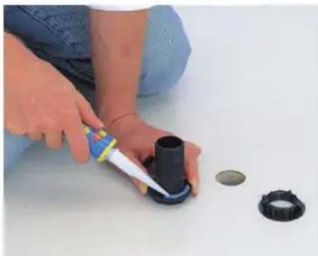 Person applying a piping bag to a black plastic tank, with other small components nearby (no text or symbols visible)