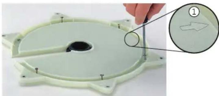 Close-up of a light green plastic mechanical component with a circular hole and mounting holes, being adjusted by a hand using a tool (no text or symbols visible)