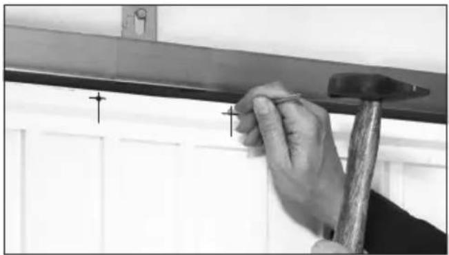 Close-up of a hand using a hammer to work on a wooden beam, with alignment markers (no text or symbols visible)