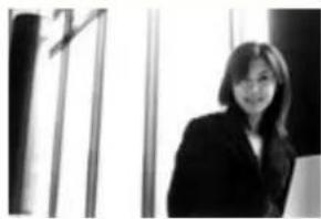 Black-and-white photo of a woman in business attire standing indoors near a window (no visible text or symbols).