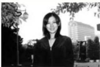 Black-and-white photo of a woman in business attire standing outdoors with trees and a modern building in the background (no visible text or symbols)