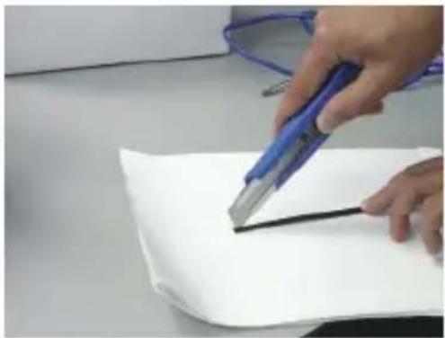Close-up of hands using a blue tool to cut a white sheet of paper (no text or symbols visible)