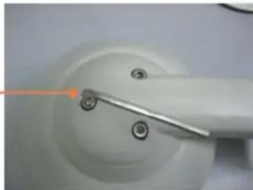 Close-up of a white mechanical component with a metal tool and screw holes, no visible text or symbols