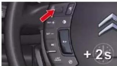 Car dashboard control panel with red arrow and '2s' indicator, showing function buttons and brand logos