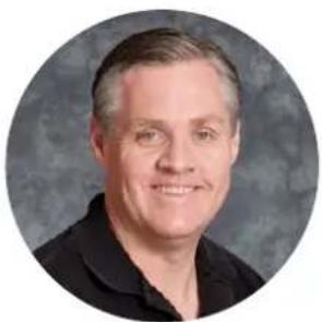 Circular portrait photo of a smiling man in a dark shirt against a gray background (no text or symbols)