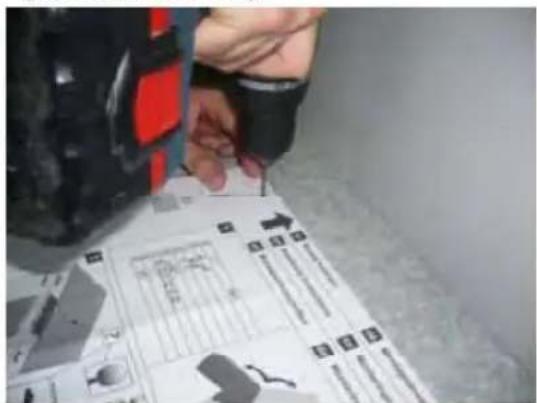 Person working on a mechanical assembly with visible components and labels, including a schematic diagram and numbered parts.