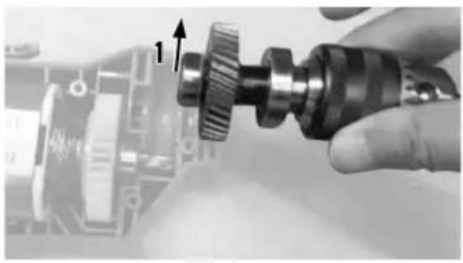 Close-up of a hand holding a mechanical gear component, with a blurred circuit board background (no visible text or symbols)