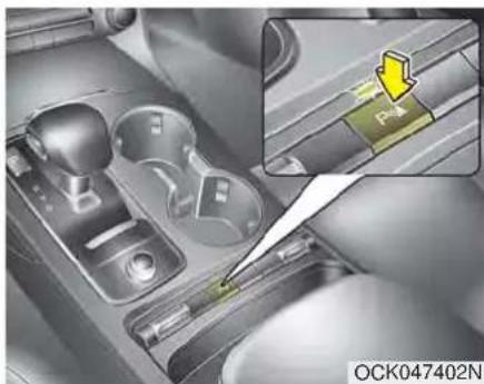 Close-up of a car interior showing a hand holding a green tool, with an inset highlighting a yellow arrow labeled 'P' (no text or symbols on the diagram itself)