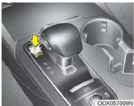 Close-up of a car gear shift lever with a yellow arrow pointing to the left side (no text or symbols visible)