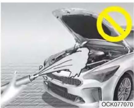 Black-and-white photo of a car with open hood and hand holding a tool, no visible text or symbols