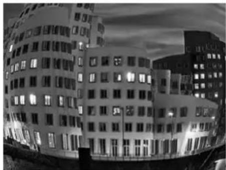 Exterior view of a modern multi-story building at dusk, illuminated by a black-and-white photo (no signage or text visible)