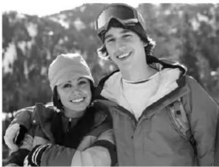 Black-and-white photo of two smiling people outdoors, one wearing a winter jacket and the other a beanie, with trees in the background (no text or symbols visible)