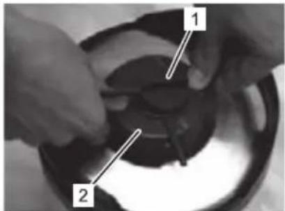 Close-up of hands assembling a mechanical component with numbered parts labeled 1 and 2