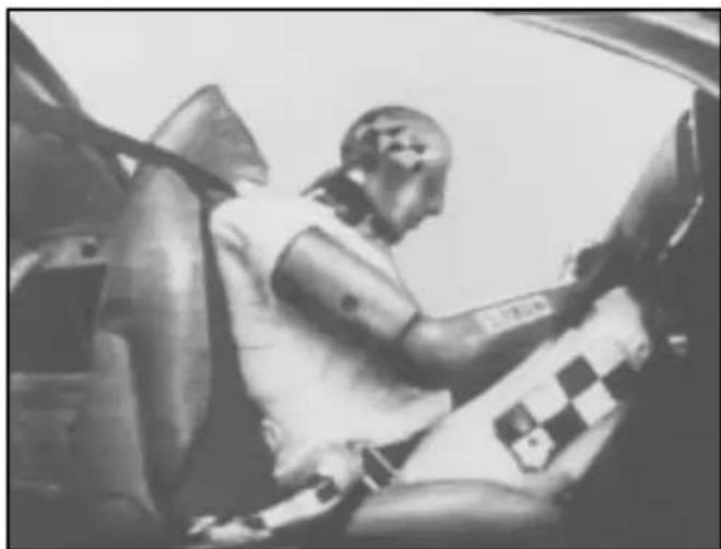 Black-and-white photo of a person seated in a car, wearing a helmet and checkered pattern (no visible text or symbols)