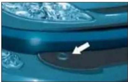 Close-up of a car's side panel with a white arrow pointing to a small circular object (no text or symbols visible)