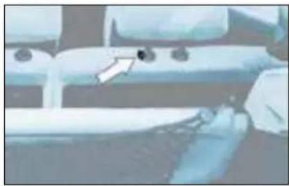 Close-up of a mechanical component with a white arrow pointing to a small dark object on a surface (no visible text or symbols)