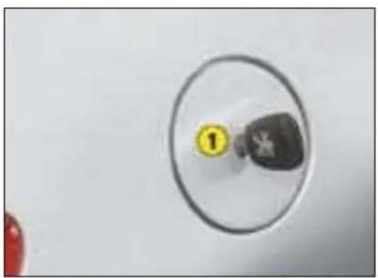 Close-up of a circular object with a numbered label (1) and a small dark object inside, against a plain background (no readable text or symbols)