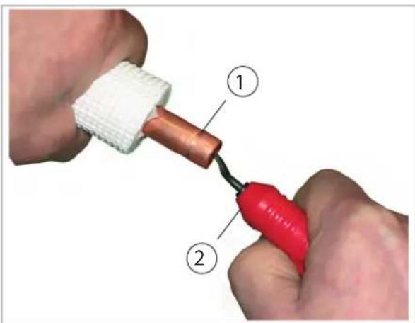 Diagram showing two hands operating a tool with labeled parts, including a copper connector and red tool.