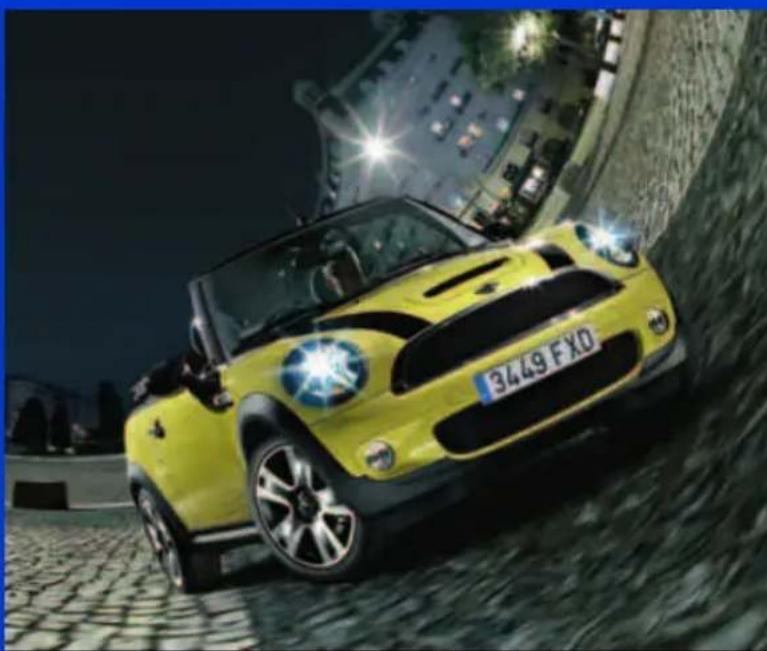Yellow Mini Cooper car driving on a cobblestone road at night, illuminated by street lights (no visible text or symbols)