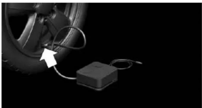 Close-up of a car tire connected to a small black electronic device with cable, against a black background (no text or symbols visible)