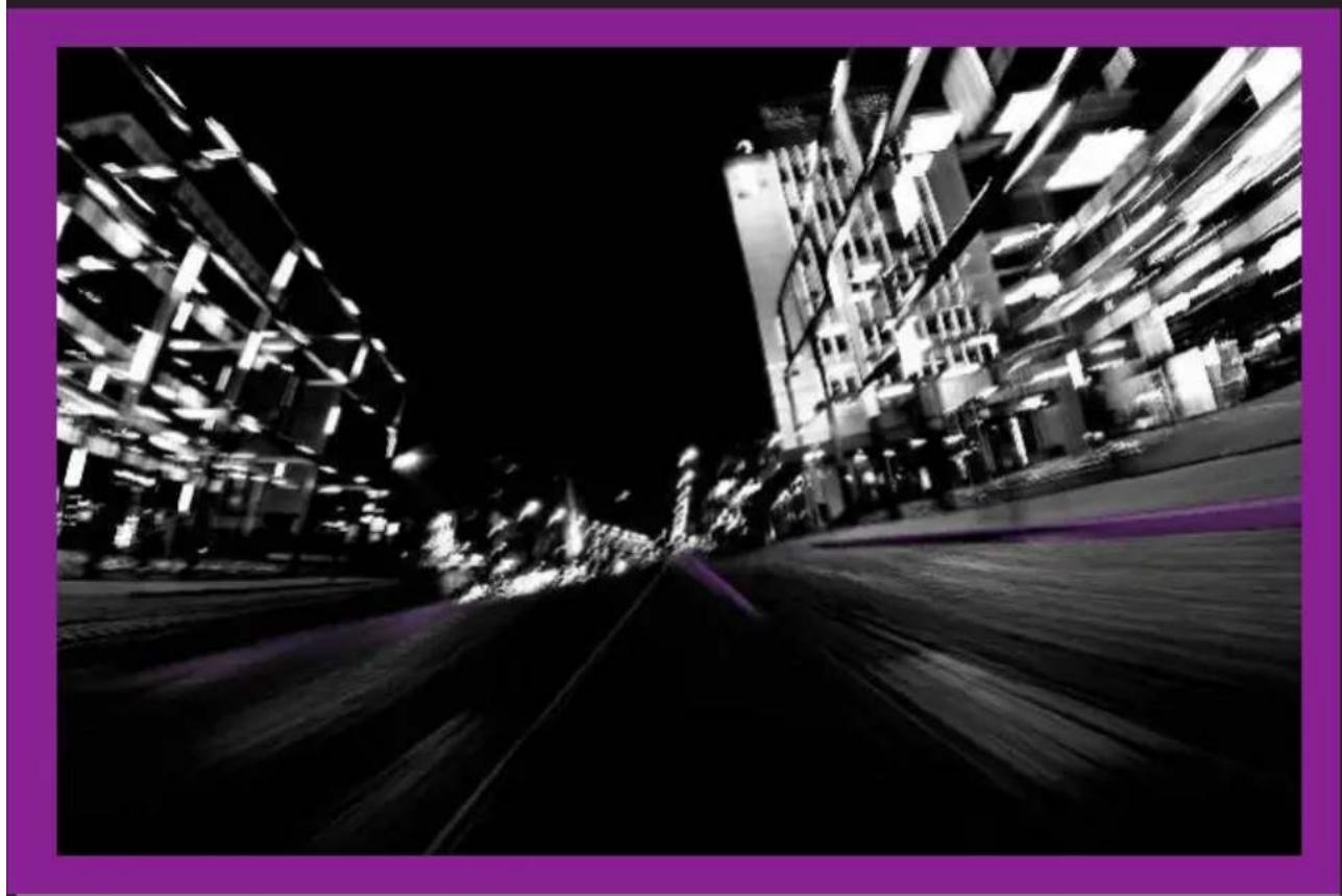 Nighttime street scene with illuminated buildings and a dark road, no visible text or signage