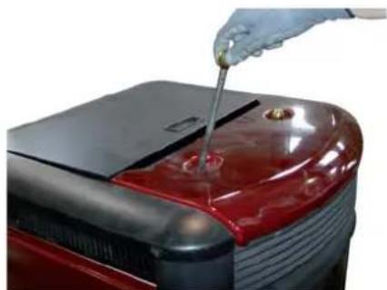 Close-up of a red car engine burner with a hand using a screwdriver to apply material (no visible text or symbols)
