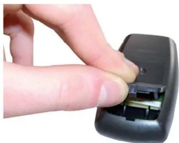 Close-up of a hand inserting a black plastic component into a black remote control case (no text or symbols visible)