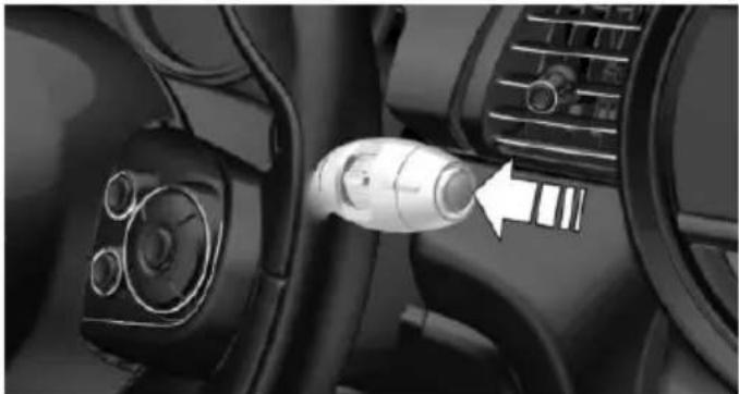 Close-up of a car interior showing a plug inserted into the dashboard with a white arrow pointing to it (no text or symbols visible)